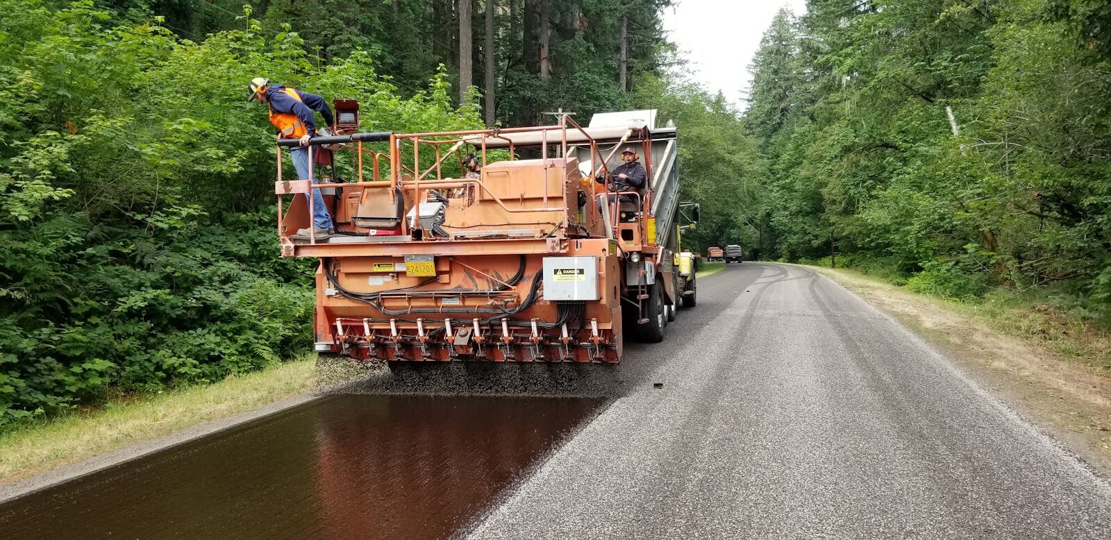 Chip seal aggregate spreader laying cover stone on tack