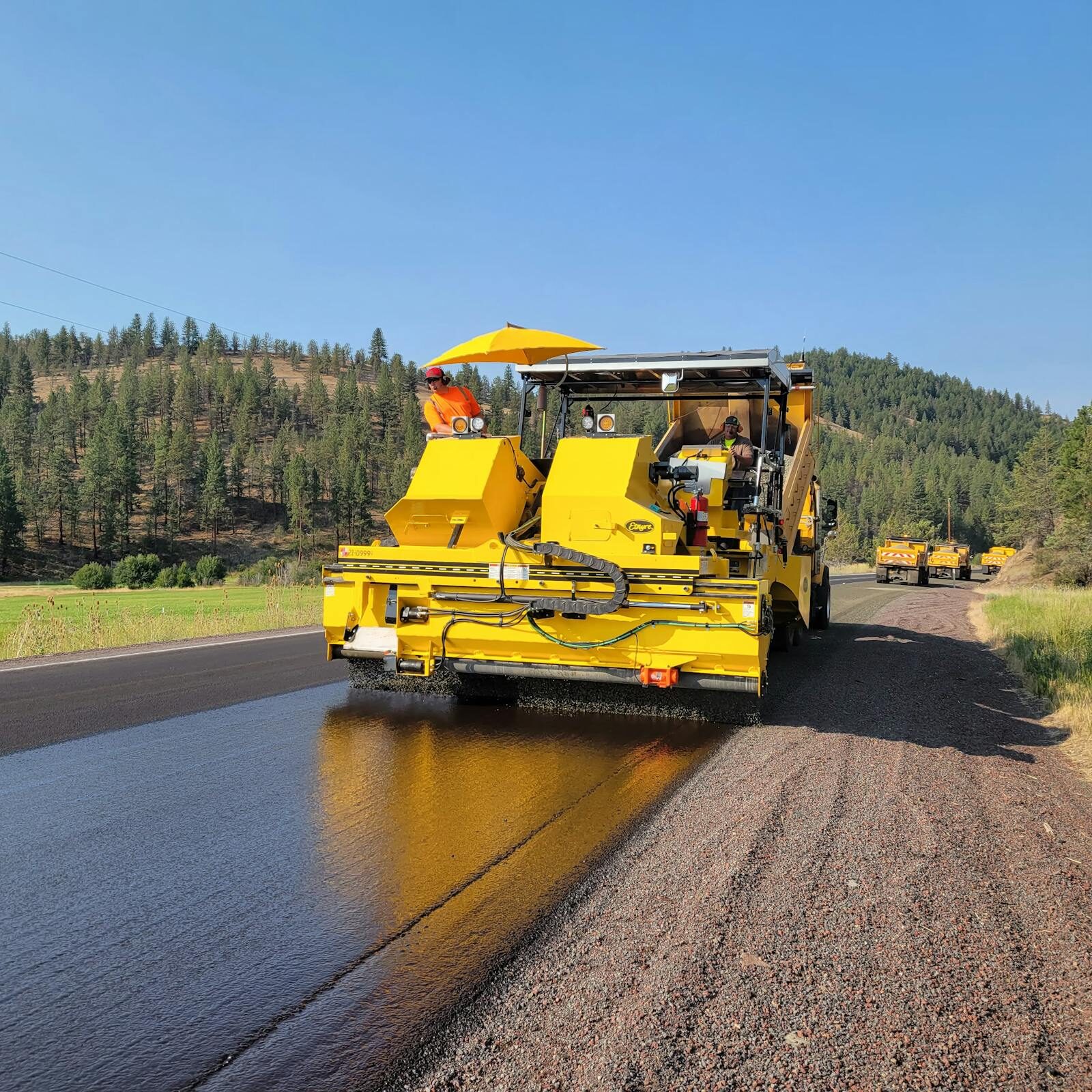 Yellow paver laying fresh asphalt overlay on rural road