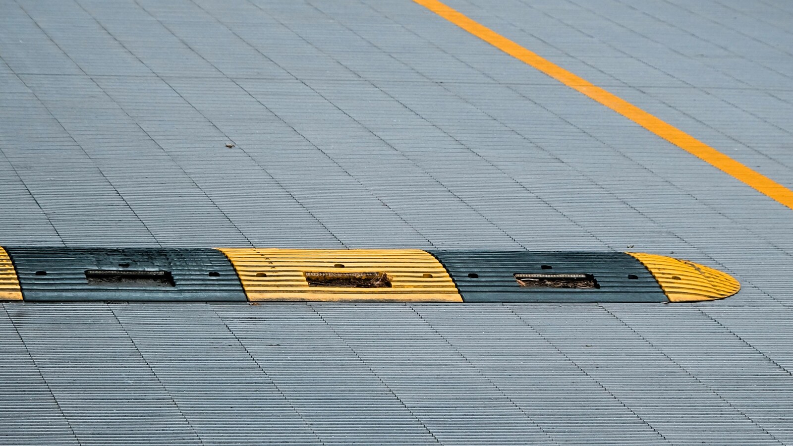 Yellow and black rubber speed hump installed across a commercial carpark lane with line marking