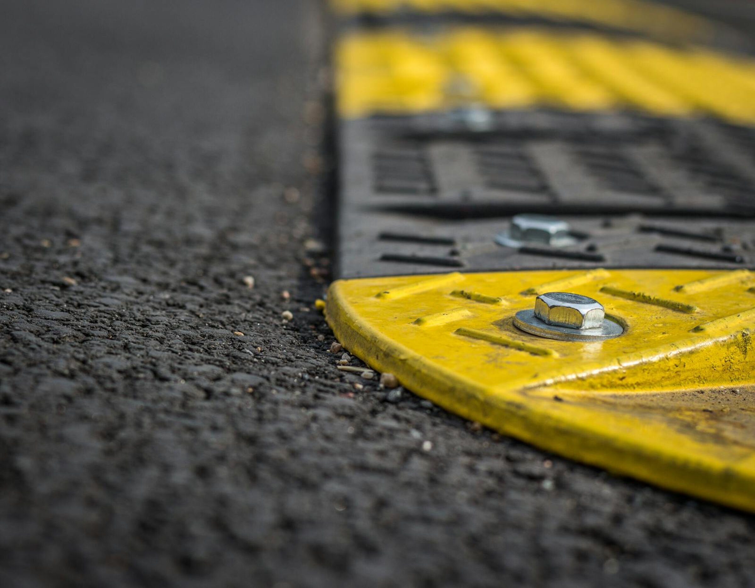 Close-up of yellow and black rubber speed hump bolted to asphalt road surface