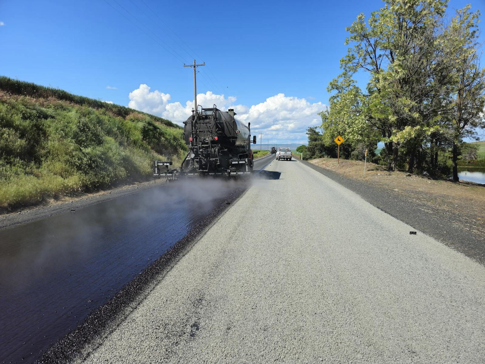 Distributor spraying bitumen on rural road β two-coat seal